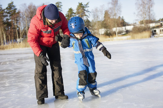 Mother helping boy ice skating on frozen lake or river