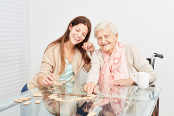 Seniorin spielt mit einer Pflegehilfe Domino