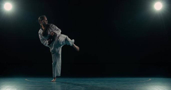 young asian girl trains martial arts taekwondo, performs kicks, slow motion, black background