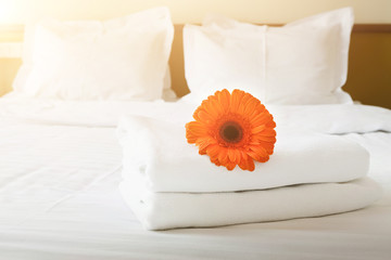 Stack of towels and flower on bed in hotel room