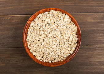 Bowl with oats next to wooden spoon on wooden table. Closeup