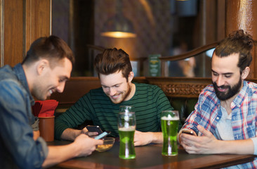 friends with smartphones and green beer at pub