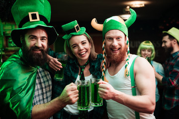 Two men and girl in carnival hats drinking beer at the bar.
