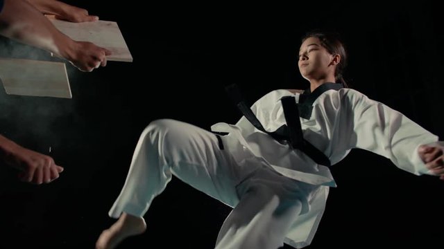 Asian beautiful girl fighter practicing to break the board with a kick of the feet, slow motion
