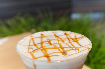 Gold caramel topping on white cream in coffee cup with green grass background.