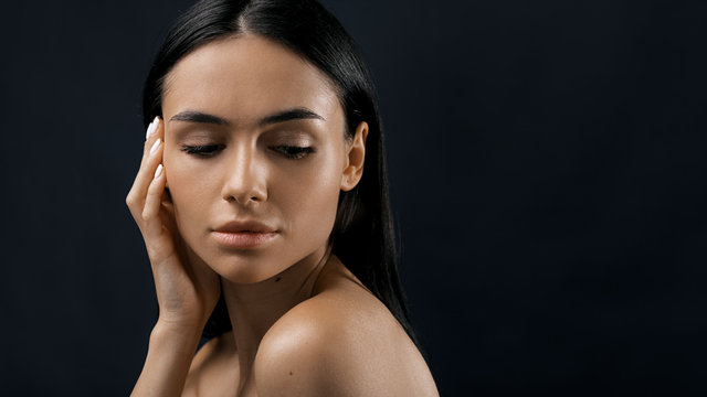 Close up portrait of a young fashion model with hand near her cheek, looking down