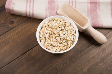 Oat flakes in a bowl next to wooden spoon.
