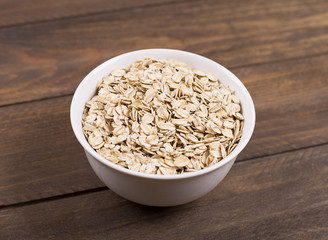 White bowl with oats on wooden table.