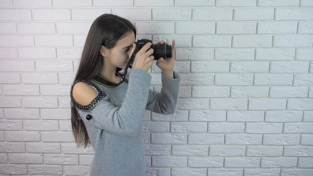The girl is a photographer. Girl with a camera on a brick wall background.