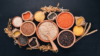 Set of Groats and Grains. Buckwheat, lentils, rice, millet, barley, corn, black rice. On a black background. Top view. Copy space.