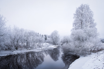Winter landscape with frosty trees and peaceful river at evening in Finland