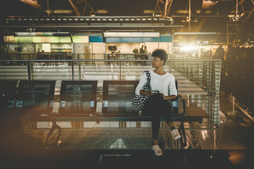 Beautiful young Black female tourist is sitting inside of modern airport terminal and waiting for her flight; cute Brazilian girl with curly Afro hair is sitting in waiting hall of railway station - Powered by Adobe