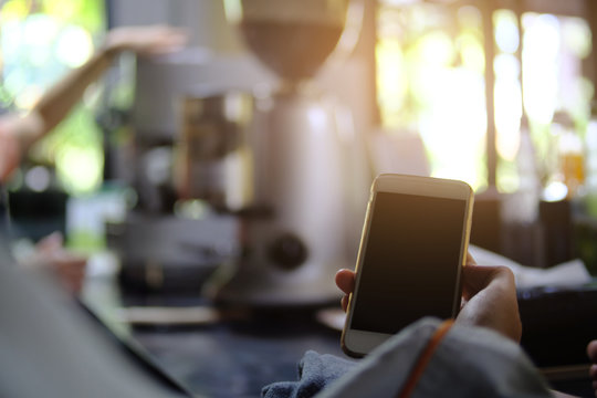 Hand hold smart phone of empty screen in coffee cafe, blurred coffee shop background