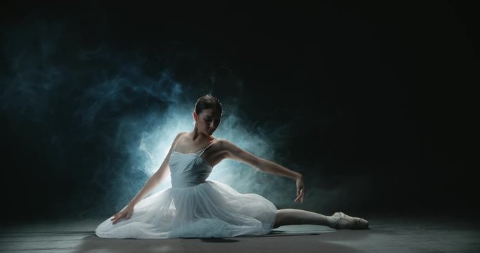 Ballerina performs elements of classical ballet in the studio, black background, smoke, slow motion