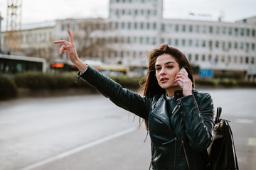 Beautiful young woman catching a taxi while talking on smartphone.