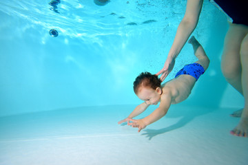 The kid dives to the bottom of the pool, and the coach helps him. Portrait. Horizontal orientation