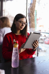 Happy young woman drinking lemonade / iced tea and using tablet computer in a coffee shop