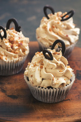 cupcakes with cream sprinkled with grated nuts on a wooden cutting board.