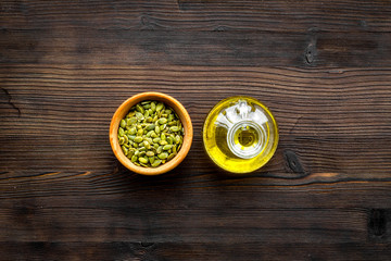 Oil for skin care. Pumpkin seed oil near pumpkin seed on dark wooden background top view copy space
