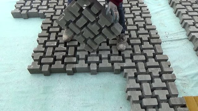 Construction workers laying interlocking paving concrete onto sheet nonwoven bedding sand and fitting them into place.