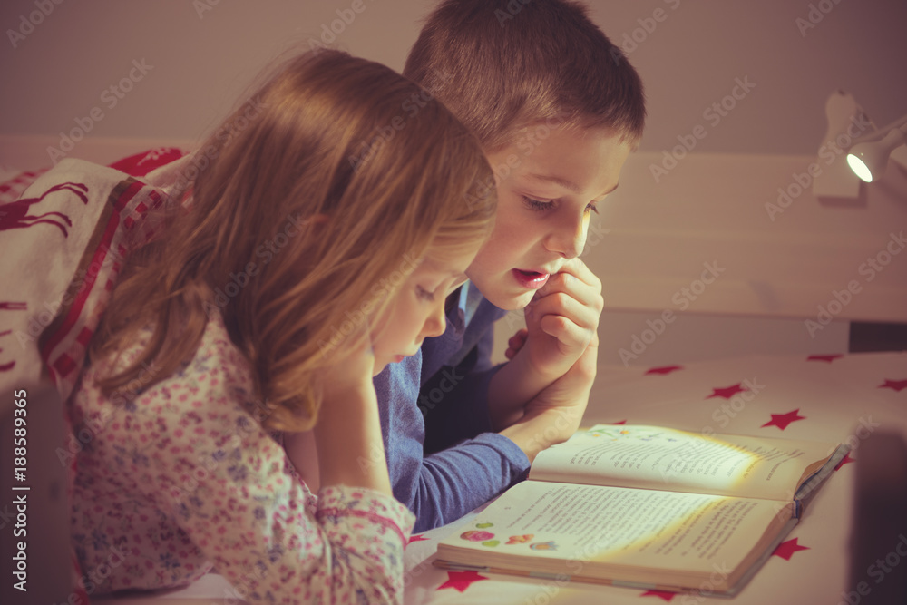 Wall mural two happy sibling children reading book in bunk bed under blanket