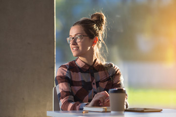 Young female girl student having coffee break in glass interior
