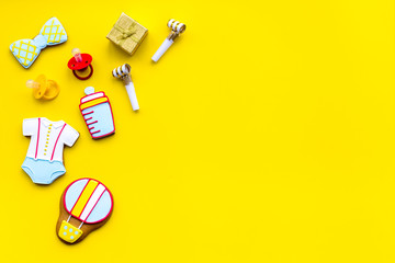 Celebrate birthday of a little baby. Cookies in shape of accesssories for child and gift box on yellow background top view copy space