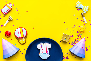 Baby shower. Cookies in shape of accesssories for child, party hats and confetti on yellow background top view copy space