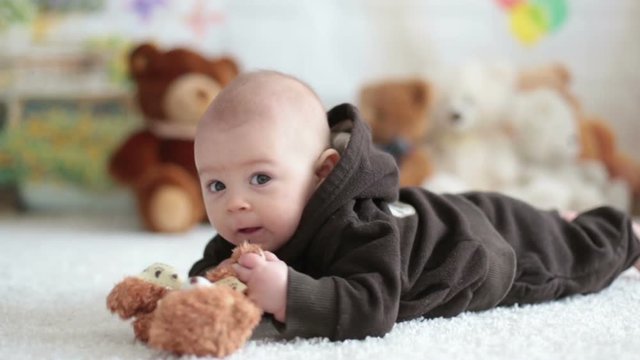 Little baby boy playing at home with soft teddy bear toys, lying down