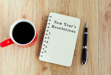 New Year's Resolutions text on notepad with pen and a cup of coffee, wooden background