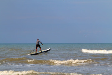 Fototapeta premium Standup paddle board surfer (SUP) surfing has caught the wave and has fun surfing on wave of Black Sea against the background of dark blue stormy sky