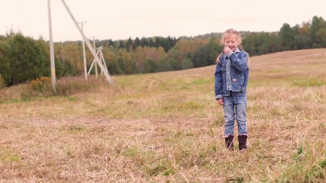 little girl in a denim suit stands in the field and looks at the camera