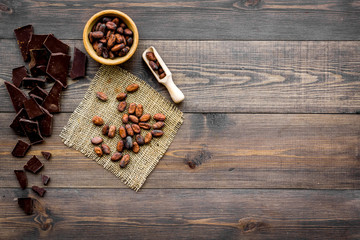 Main ingredient for chocolate. Cocoa beans near pieces of chocolate on dark wooden background top view copy space