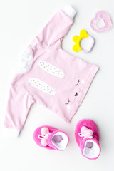 Cute pink baby clothes for girl. Shirt, booties, toy, bottle on white background top view copy space