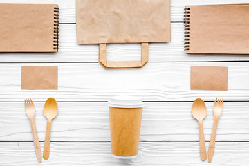 Set of recycle brown paper bag, disposable tableware cup, spoon, fork, notebook on white wooden background top view pattern