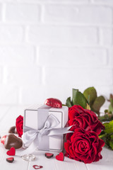 Fresh red roses and gift box on wooden table