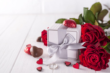 Fresh red roses and gift box on wooden table