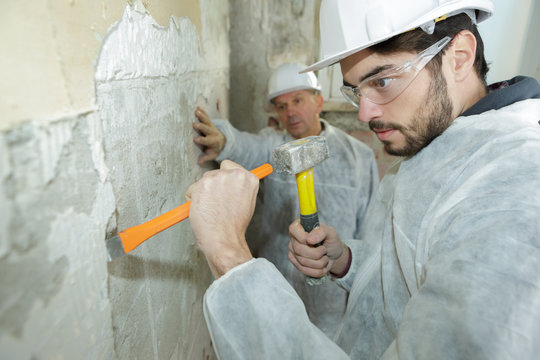 builders using a hammer to remove walls plaster
