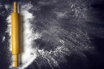 Rolling pin and white flour on a dark background. Free space for text .