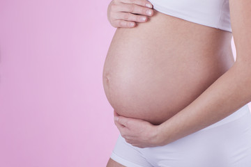 The picture of baby bump isolated on pink background. The happiness of waiting for a new family member.