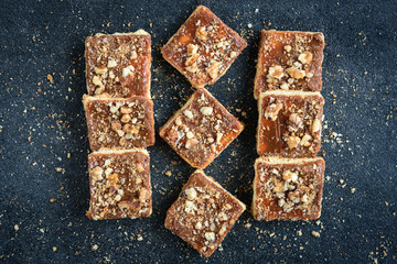 Homemade caramel shortbread squares cookies with nuts on black background with crumbs.