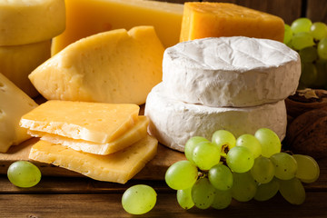 Various types of cheese on dark rustic wooden background.