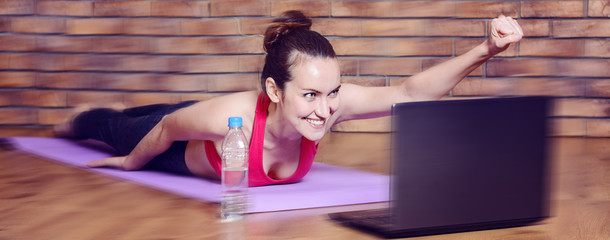Young smiling woman lying on fitness Mat depicts the flight of a superhero during the warm-up...
