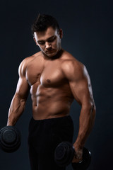 Fototapeta na wymiar Muscular bodybuilder doing exercises with dumbbell over black background.Strong athletic man shows body,abdominal muscles,biceps and triceps.Work out,gaining weight,pumping up muscles with dumbbells.