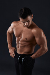 Fototapeta na wymiar Muscular bodybuilder doing exercises with dumbbell over black background.Strong athletic man shows body,abdominal muscles,biceps and triceps.Work out,gaining weight,pumping up muscles with dumbbells.