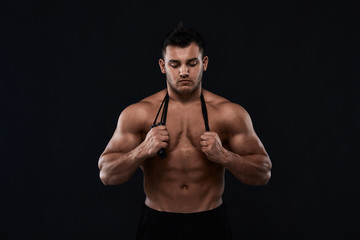 Fototapeta na wymiar Muscular bodybuilder with jump rope on black background.Strong athletic man shows body,abdominal muscles,chest muscles,biceps and triceps.Work out,gaining weight. Bodybuilding concept.