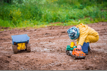 the boy in yellow suit playing with a toy car in the dirt