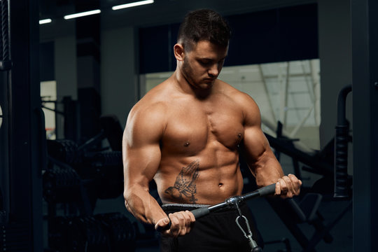 Muscular bodybuilder doing exercises on cable crossover machine in gym.Strong athletic man shows body,abdominal muscles,biceps and triceps.Work out,gaining weight,pumping up muscles.