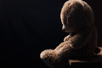 A lone Teddy bear sitting in the dark, side view,