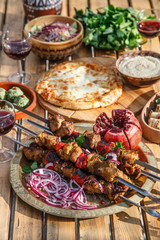 Meat shish kebab on a plate with onions, pomegranate seeds, hot pepper, wooden backdrop background